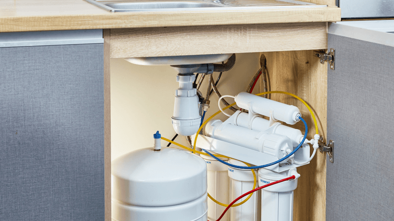 Under-sink reverse osmosis system installed in a kitchen cabinet, showing the compact unit and dedicated drinking water faucet