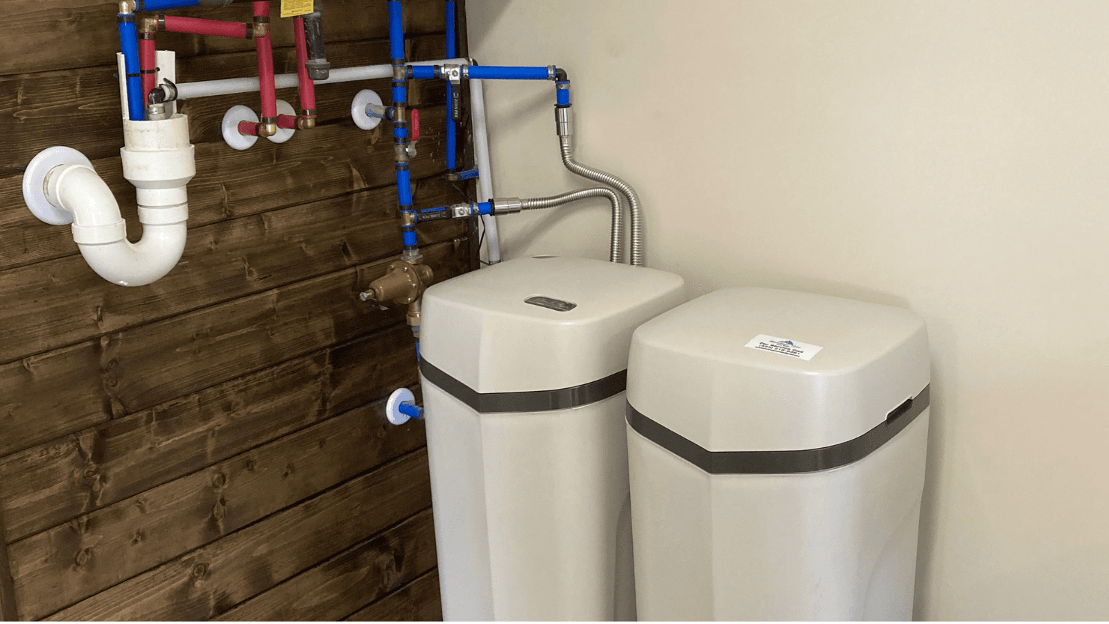 Professional whole-house water treatment system installation in a home utility room, showing a water softener and pre-filter staged neatly next to a water heater